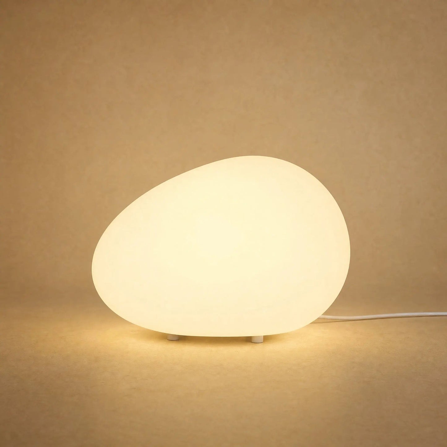 Edlen pebble table lamp lit in warm white against a sandy mineral backdrop | Wickleigh