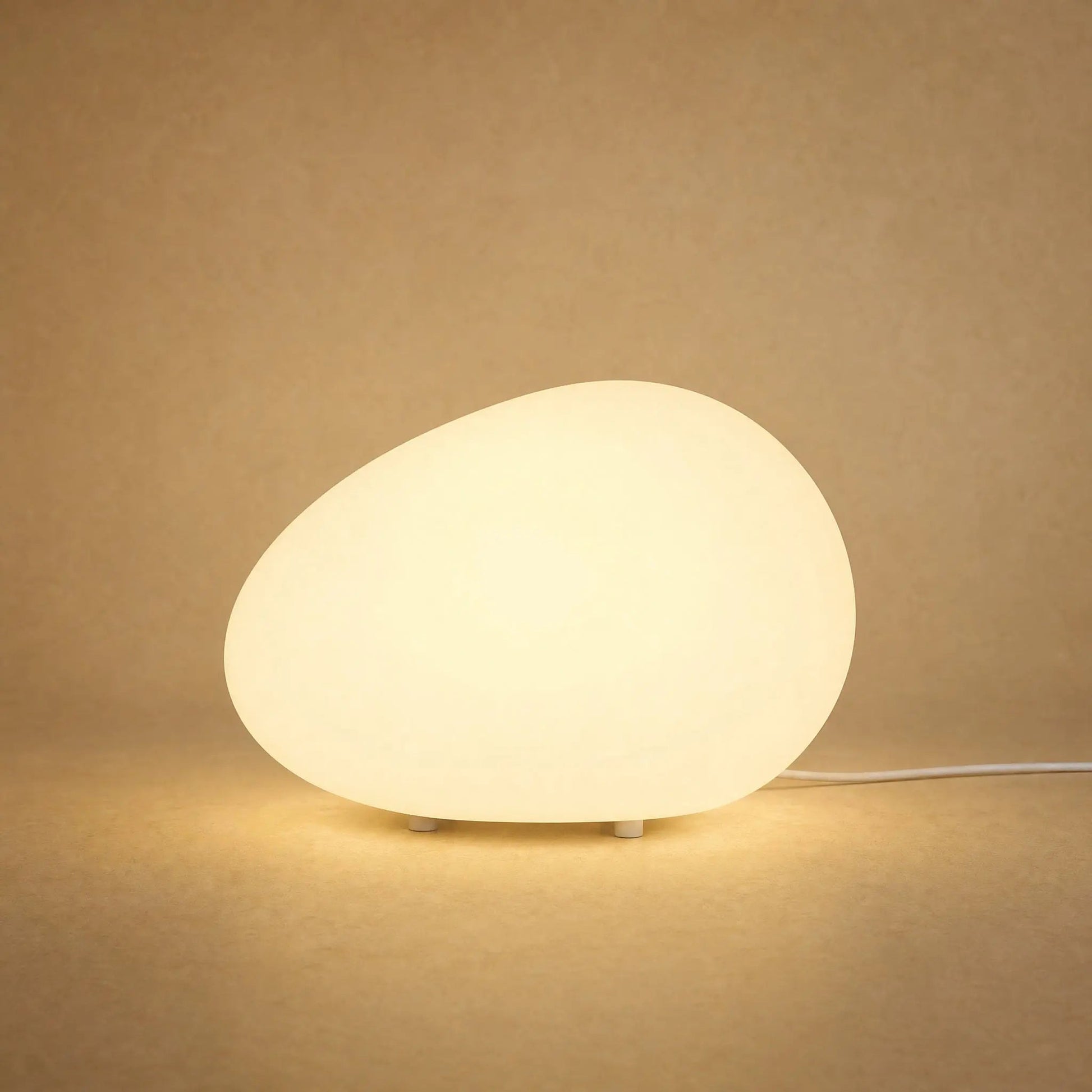 Edlen pebble table lamp lit in warm white against a sandy mineral backdrop | Wickleigh