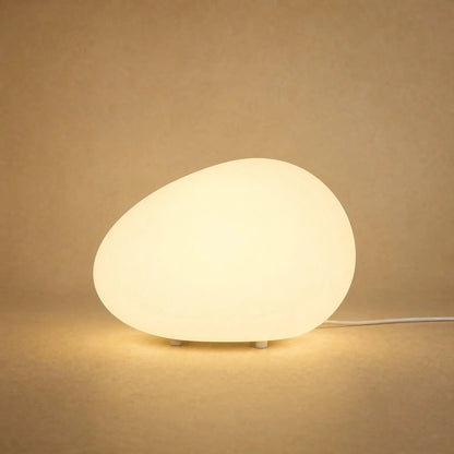 Edlen pebble table lamp lit in warm white against a sandy mineral backdrop | Wickleigh