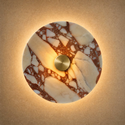Belna Art Deco wall light, amber veined stone disc with gold metal hub, lit | Wickleigh