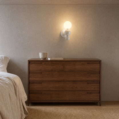 Brelin white ball wall light lit above a walnut chest of drawers in a bedroom | Wickleigh
