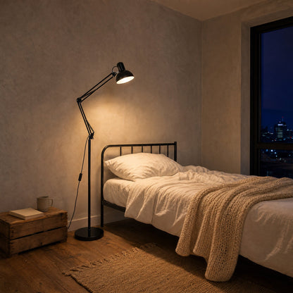 Melen black floor reading lamp lit above a bed in a small studio flat at night | Wickleigh