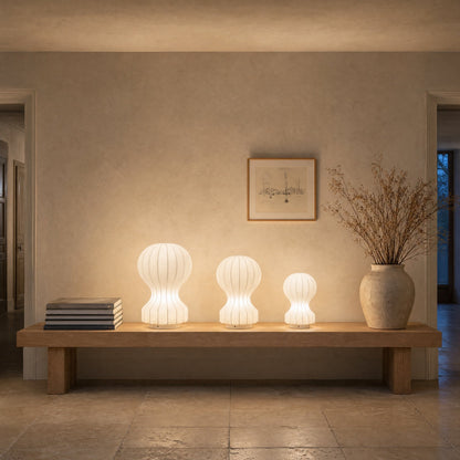 Three Pyrren cocoon table lamps lit, lined up on an oak bench | Wickleigh