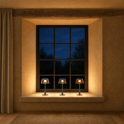 Three Tylen rechargeable table lamps, clear, smoked grey and amber, lit in a row on a windowsill | Wickleigh