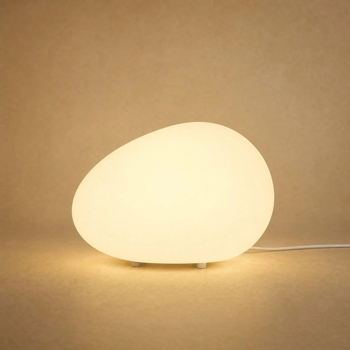 Edlen pebble table lamp lit in warm white against a sandy mineral backdrop | Wickleigh
