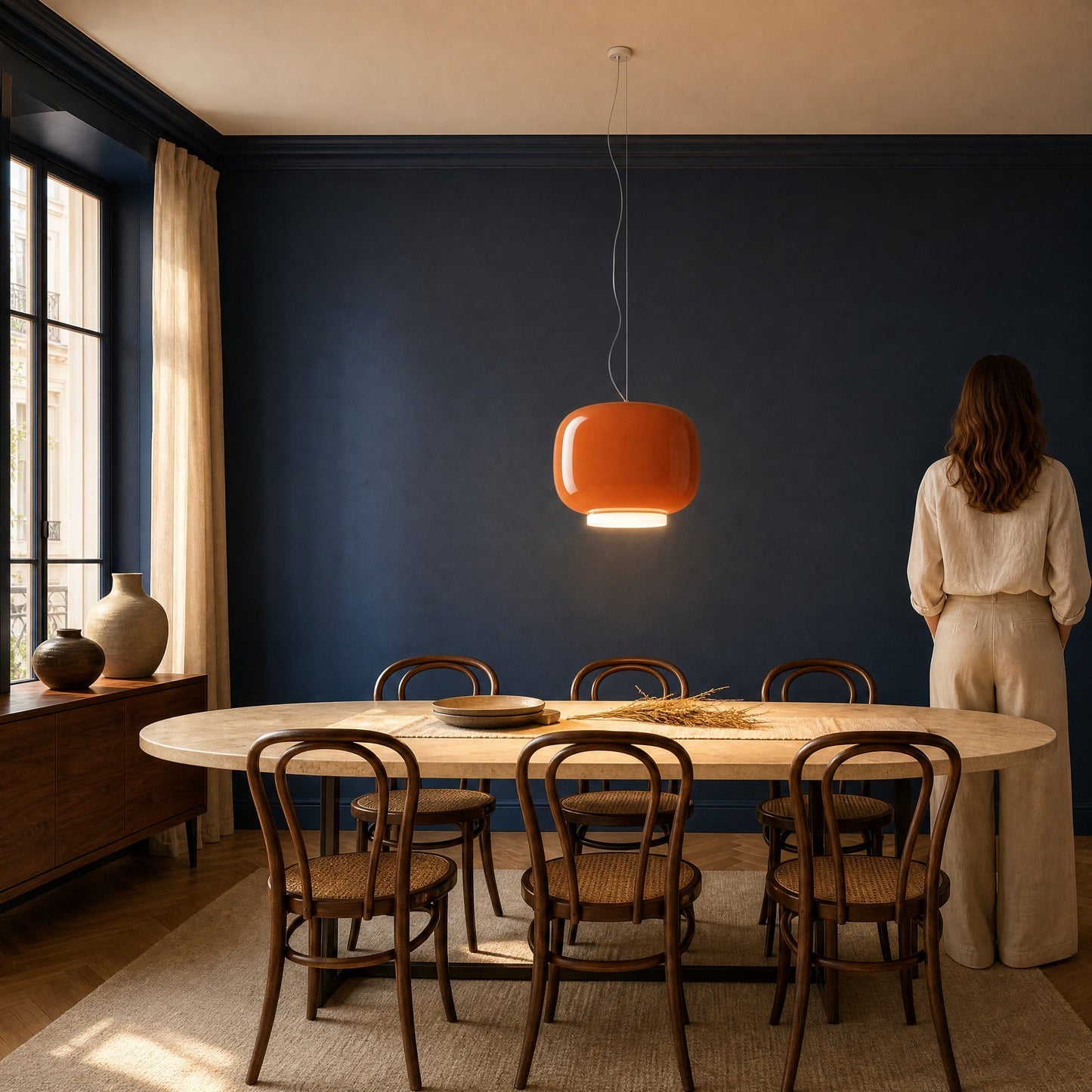Ulvin amber pendant light switched on above an oval travertine dining table | Wickleigh