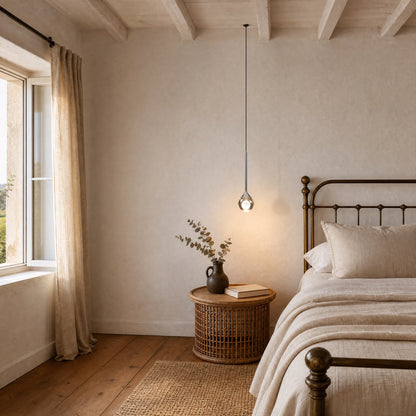 Falen smoked glass pendant light lit above a rattan bedside table in a country-style bedroom | Wickleigh
